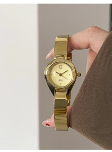 Detailed close-up of a luxury gold bangle watch with a minimalist round dial on a wrist