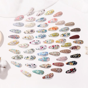 Lot de 50 barrettes BB en tissu floral disposées en forme de cœur sur un fond de tissu blanc