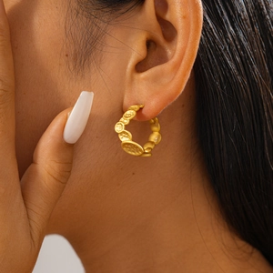 Close-up of a gold geometric C-shaped earring with textured irregular hammered finish
