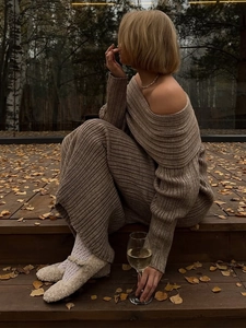 Detail of a brown ribbed knit off-shoulder dress with white fuzzy flats on autumn deck