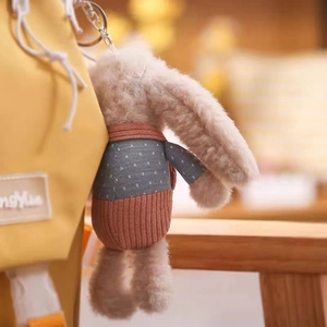 Close-up of plush rabbit keychain with blue polka dot sweater on a yellow backpack