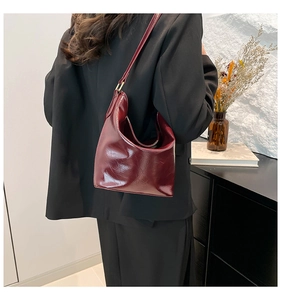 Burgundy wrinkled patent leather hobo bag worn over the shoulder by a model