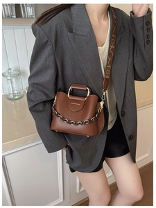 Close-up of brown leather bucket bag with gold handle and printed wide strap