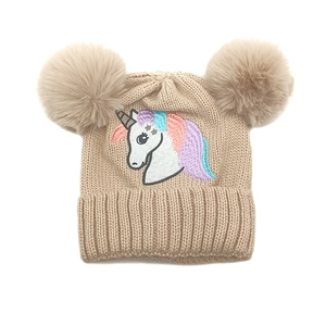 Détail de la broderie licorne et doubles pompons en fourrure sur bonnet beige