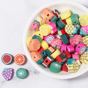 Assorted fruit-shaped polymer clay beads for DIY jewelry making in a white ceramic bowl