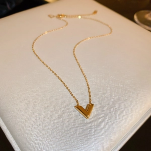Vue détaillée d'un collier doré avec pendentif en V sur un coffret à bijoux en cuir blanc