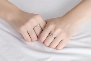 Close-up of couple's silver rings featuring a pink heart stone and a small diamond inlay