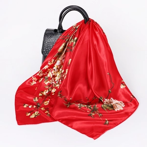 Red floral satin square scarf draped on a black leather handbag with a silky finish