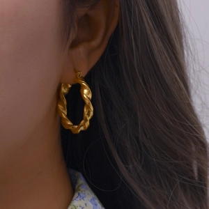 Gros plan de boucles d'oreilles créoles dorées torsadées portées par un mannequin