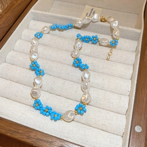 Close-up of handmade beaded floral necklace with blue petals and baroque pearls