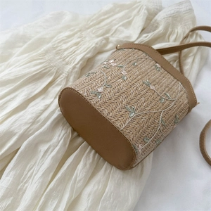 Sac seau en paille avec broderie florale et finitions en cuir sur fond de tissu blanc