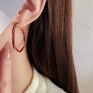 Close-up of model wearing twisted gold and burgundy enamel hoop earrings in retro style