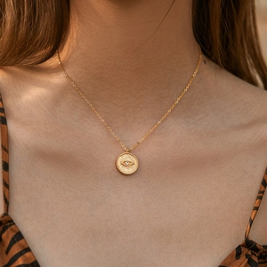 Detail of a gold evil eye coin necklace with white zircon on a bohemian pendant