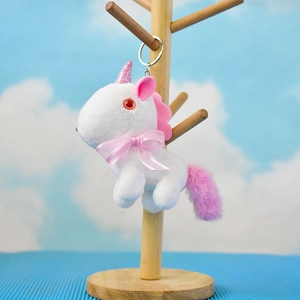 Nahaufnahme von Plüsch-Einhorn-Schlüsselanhänger mit rosa Schleife am Holzständer.