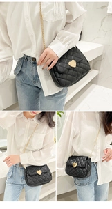 Detail of black quilted crossbody bag featuring a golden heart-shaped metal clasp and chain