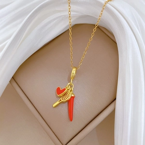 Detailed close-up of golden necklace with red heart, tennis racket, and chili pendants