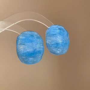 Macro detail of blue irregular resin earrings with white brushed texture and translucent finish