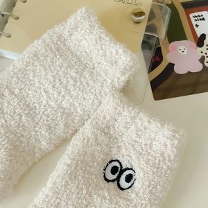 Close-up of cream coral fleece socks with cute cartoon eye embroidery and plush texture