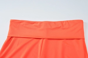 Detail view showing the wide folded waistband of vibrant orange elastic knit yoga pants