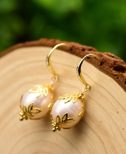 Macro detail of pink baroque pearl earrings with gold leaf frame on a natural wood surface