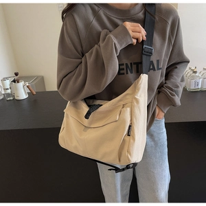 Detailed close-up of a large beige canvas messenger bag with adjustable black strap