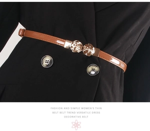 Detail of brown patent leather belt with gold flower buckle on a black dress