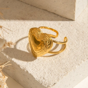 Adjustable gold heart locket ring with vintage engraved patterns on a stone background
