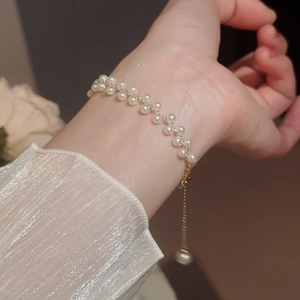 Gros plan d'un bracelet de perles tressées à double rangée sur un poignet avec chaîne dorée