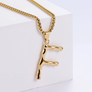 Detail of gold letter F pendant with irregular lava texture on a classic box chain