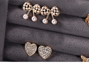 Detailed macro view of gold bow-knot pearl earrings and heart-shaped rhinestone studs