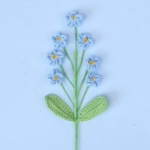 Detailed view of hand-knitted blue forget-me-not crochet flowers with green wool leaves