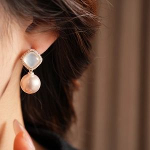 Close-up of elegant square zircon stud and large lustrous pearl earrings on model