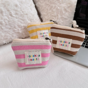 Three striped mini cosmetic pouches in pink, yellow, and brown on a soft white bed