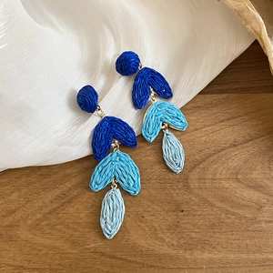 Detail of tiered blue raffia tassel earrings on a natural wood and silk background