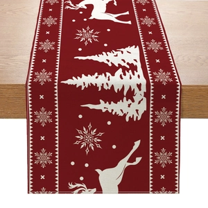 Deep red Christmas table runner with white reindeer and snowflake patterns on a wooden table