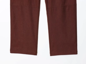 Close-up detail of dark brown cotton canvas trousers showing knee seams and stitched hems