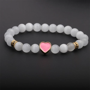 White cat eye stone beaded bracelet with gold pink enamel heart charm on black background