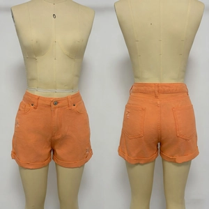 Dettaglio degli shorts in denim arancione con orli logori e risvolti su un manichino