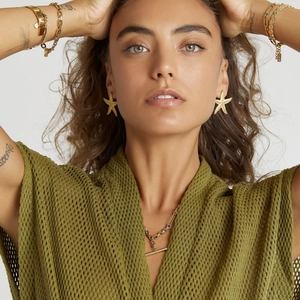 Close-up of a model wearing a gold starfish earring and layered gold chain jewelry