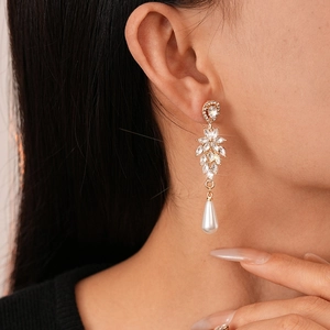 Elegant gold drop earrings with diamond leaves and teardrop pearls on a female model