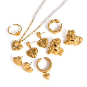 Conjunto de joyas corazón dorado con collar de perlas, pendientes y anillos sobre fondo blanco