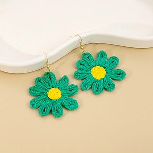 Détail des boucles d'oreilles marguerites tissées main aux pétales verts et cœur jaune