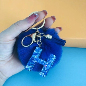 Close-up of blue pompom keychain with sequin letter H charm and gold lobster clasp
