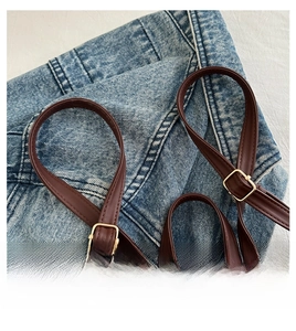 Detail of adjustable dark brown leather shoulder strap with gold buckle on denim fabric