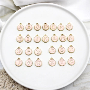 Detailed view of pink enamel alphabet charms on gold alloy discs for DIY jewelry