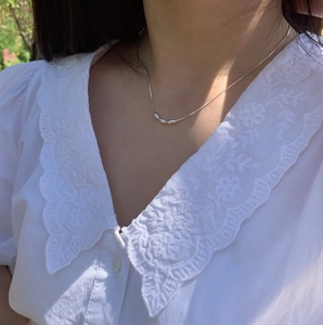 Detail view of silver snake chain necklace with small beads worn on lace clothing