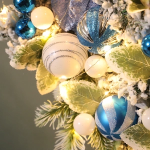 Close-up of blue and white Christmas ball ornaments with pine needles and warm LED lights