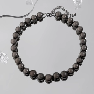 Detailed shot of black bead necklace with metal clasp on a reflective mirror background