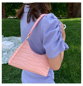 Pink crocodile pattern hobo bag worn by a model on a shoulder against a green lawn background