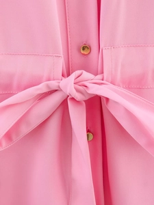 Detail of pink drawstring shirt with a golden button and textured fabric texture